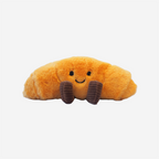 Plush toy shaped like a croissant with a smiling face on a white background