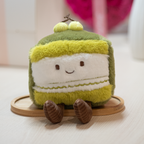 Plush toy resembling a slice of matcha cake with a green top on a wooden stand.