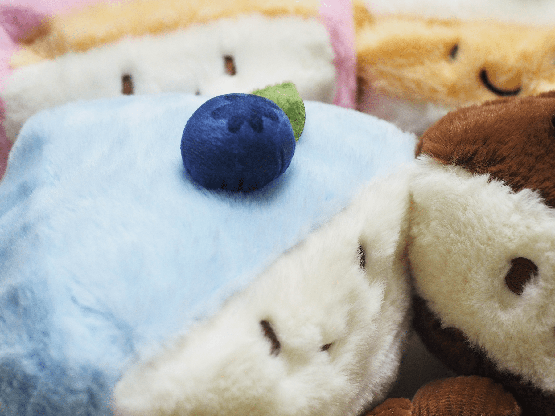 Close-up of a plush toy with a blueberry on top, surrounded by other plush items.