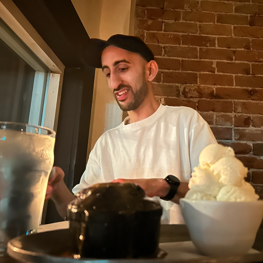 Man sitting at a table with a slice of cake and a glass of water in a casual setting.