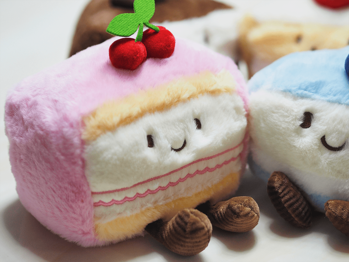 Two plush toys resembling cake slices with faces on a white background